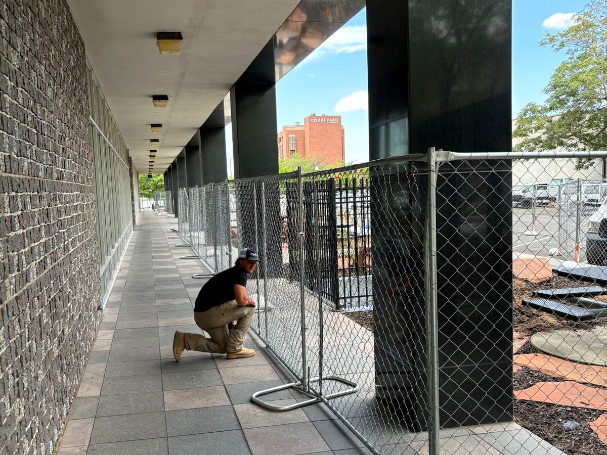 RPS crew member setting a chain link fence panel along a downtown sidewalk