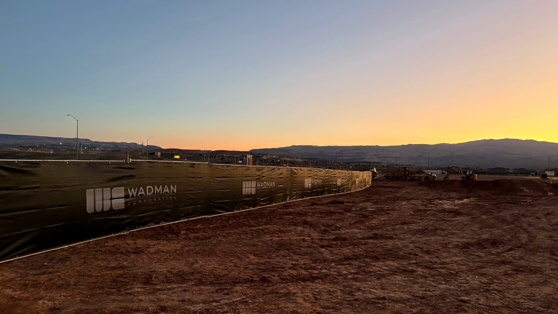 Branded privacy screen on temporary fence wrapping a commercial dirt pad at sunset