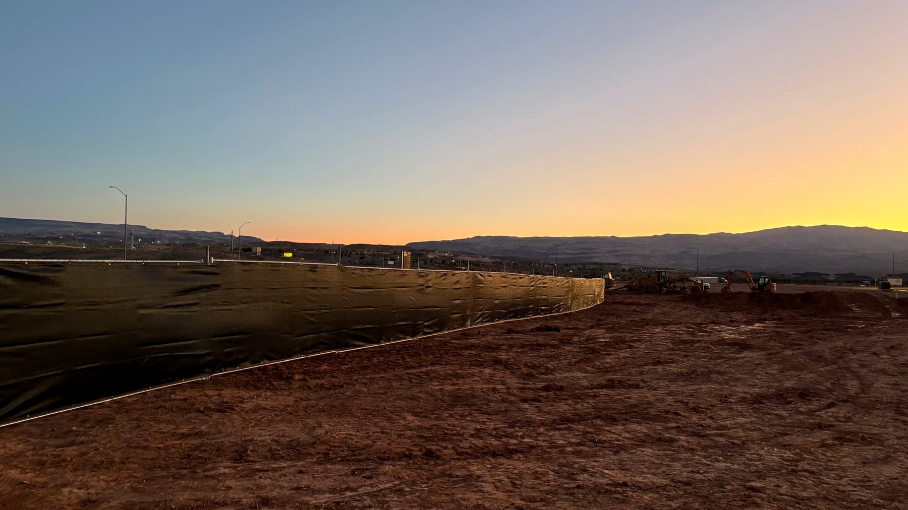 Privacy-screened temporary fence enclosing a commercial jobsite at sunset